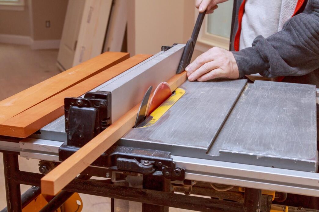 Woodworker using a table saw with safety gear in a sunlit workshop.