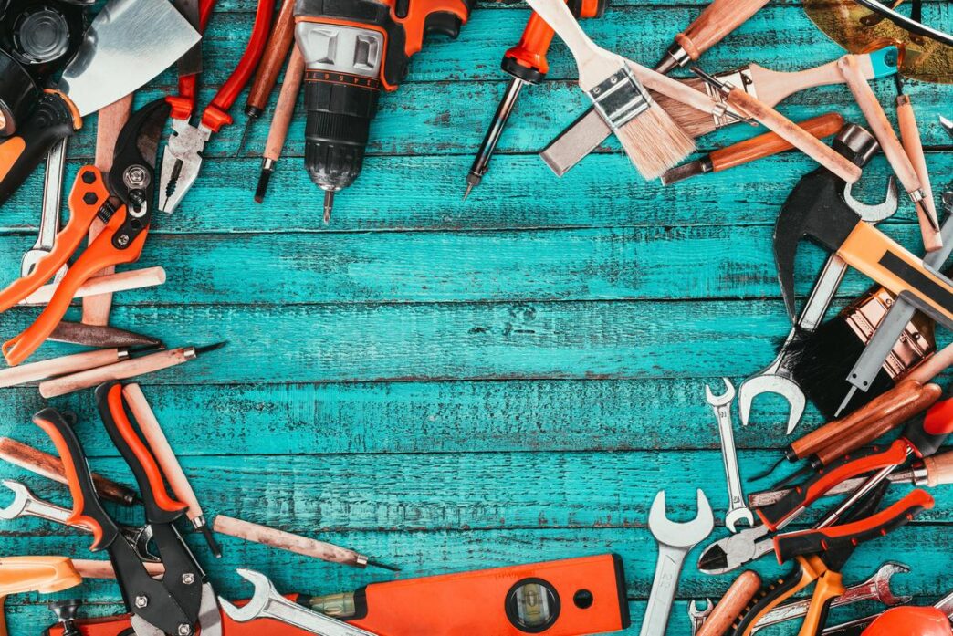 Assorted home repair tools on a rustic workbench with sunlight highlighting their textures.