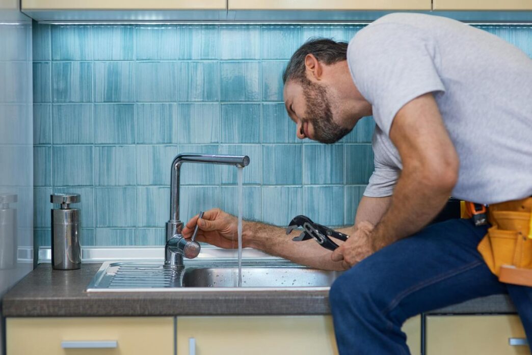 A close-up of a hand repairing a leaky faucet in a modern kitchen.